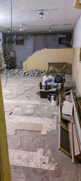 Demolition work and cleaning out to prepare for construction in long narrow room. Debbris and other junk visible showing bricks in pile and partial floor tiles