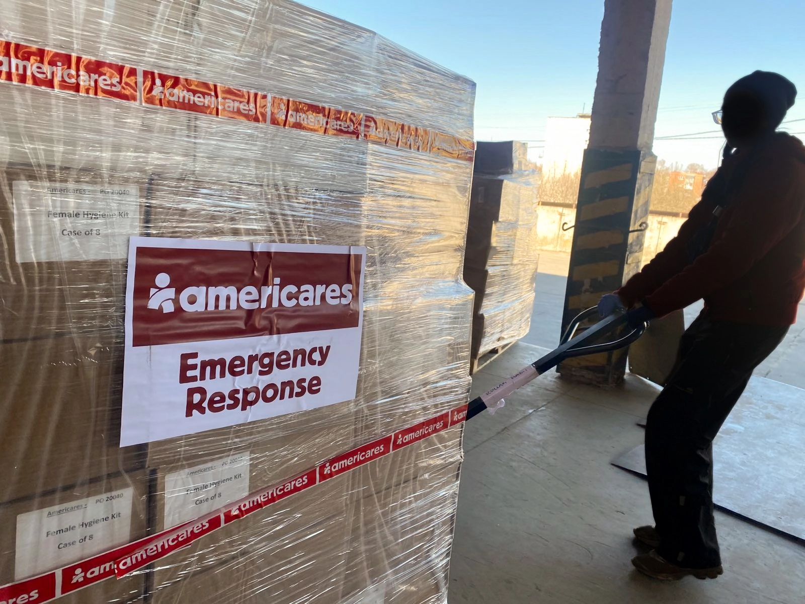 silhouette of worker moving palette of emergency response supplies with americares emergency response branding on the shipment wrapping.