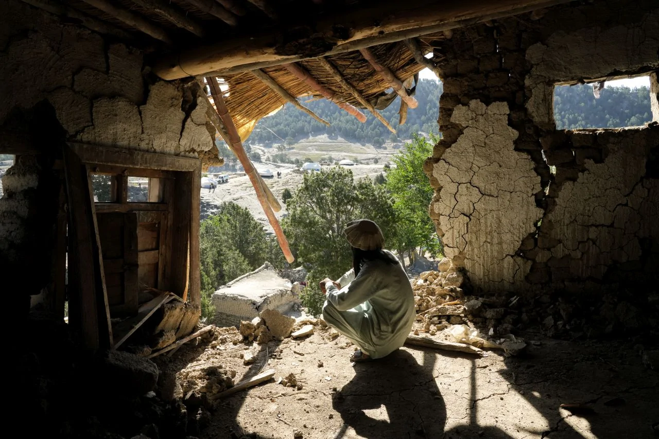 Person in white garmnt huddles in remains of home after earthquake in Afghanistan