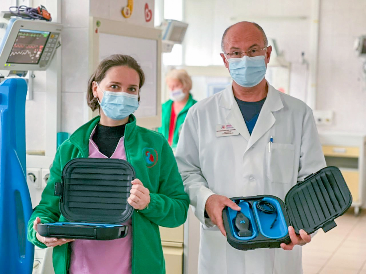 Two doctors, one in green jacket over pink scrubs and one in white lab coat, both masked holding iQ probes in their cases.