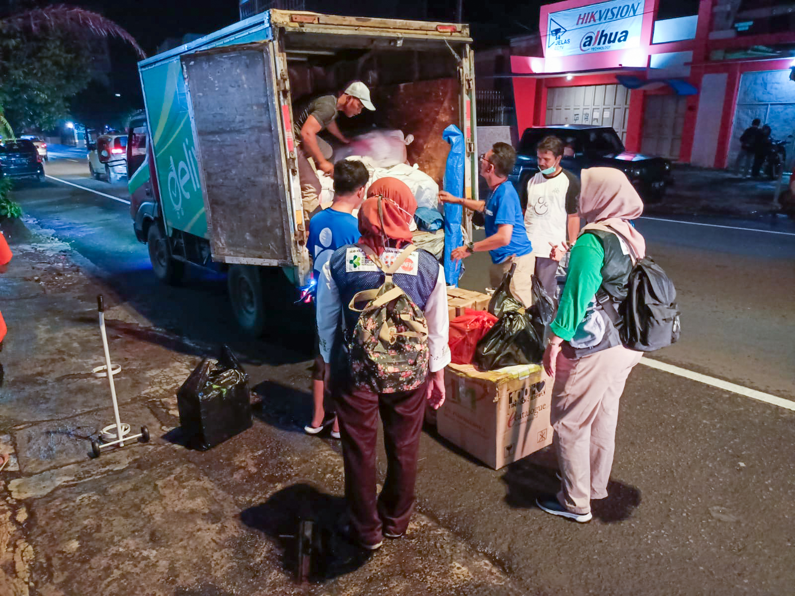 Two Americares staff members in blue t-shirts work with four other people (one inside van) unloading supplies from a box van.