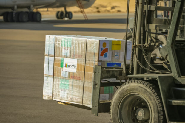 Fork lift is carrying shipment with Anera and Americares branding visible toward a cargo plane in background.