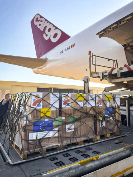A shipment in net and loading platform awaits load into cargo plane with tail of plane and part of cargo door visible.