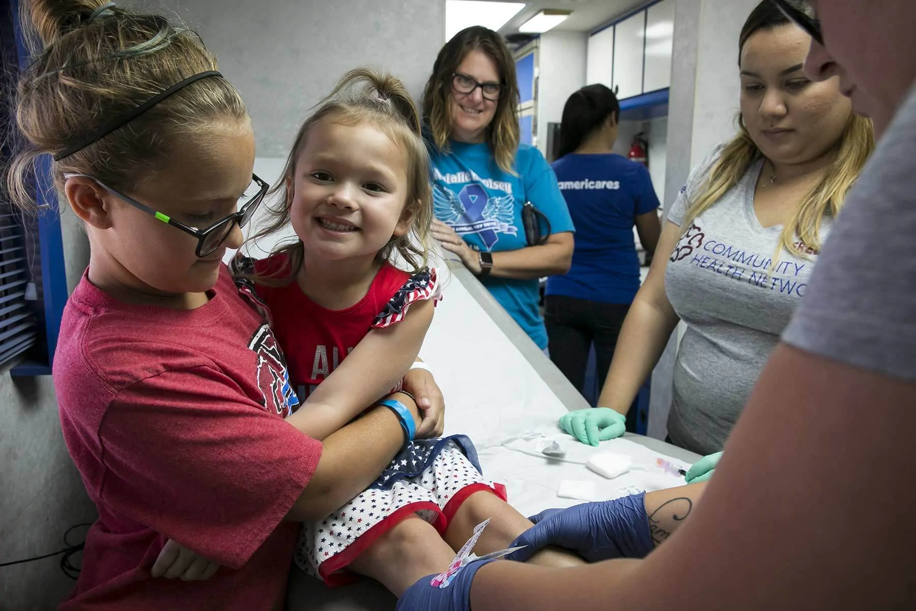 A little girl gets treatment at an Americares clinic while her older sister comforts her.