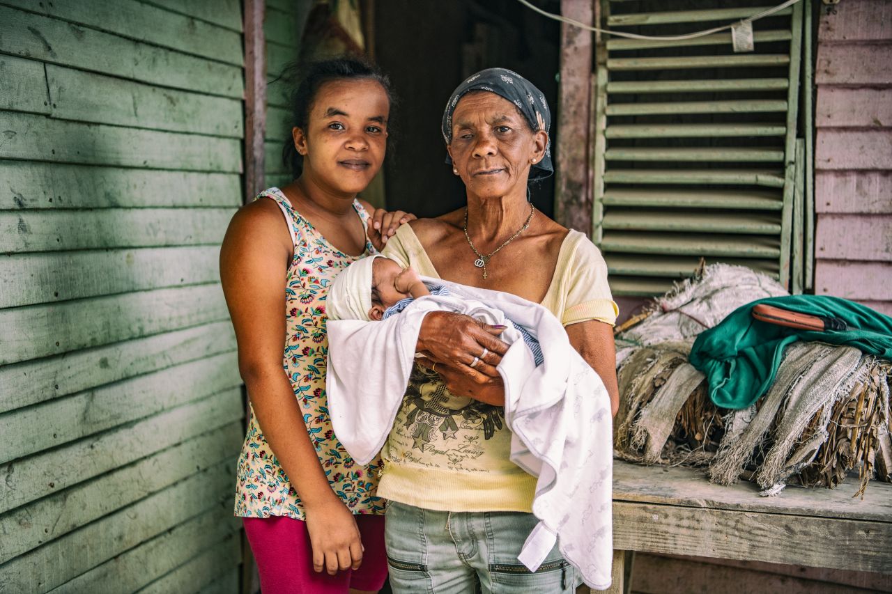 grandmother holding grandchild with mother beside them