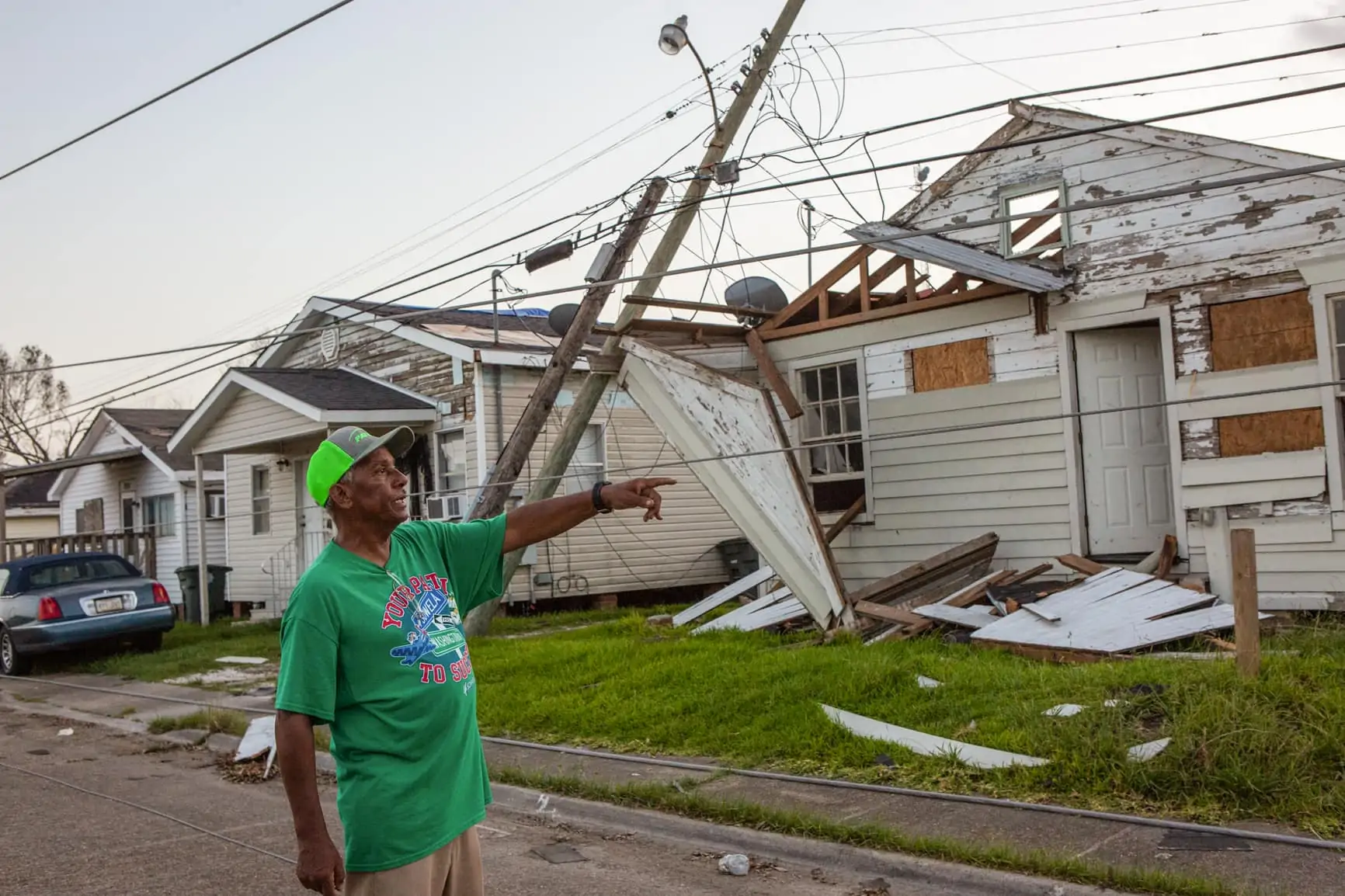 Michael H. Captain Sr. points to the damage created by Hurricane Laura on his street with damaged houses and a down telephone pole behind him.