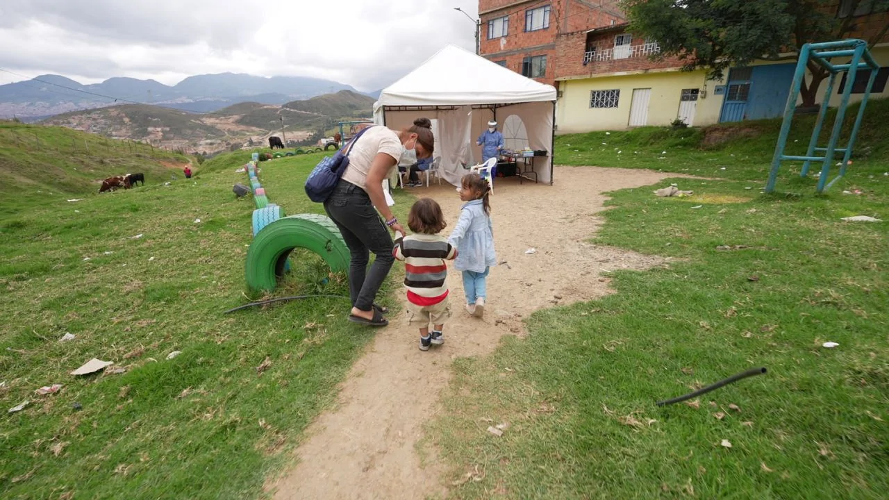 Two children with mother walking up path to a mobile health clinic in Bogota, Colombia, March 4, 2022. (Photo - Jeff Kennel/Americares)