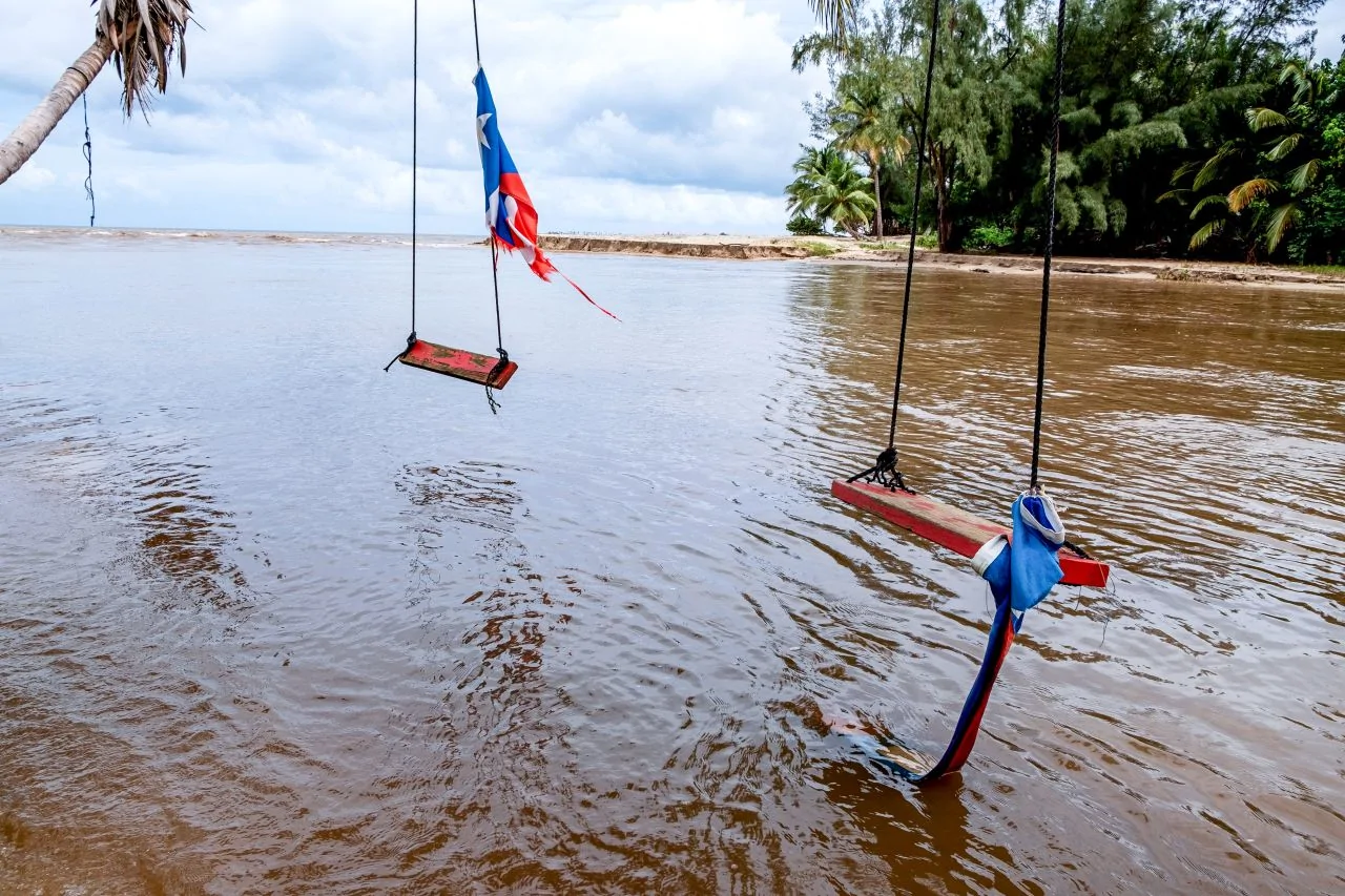 Puerto Rico flag remnants tied to wooden swings hanging over floodwaters covering a recreational area.