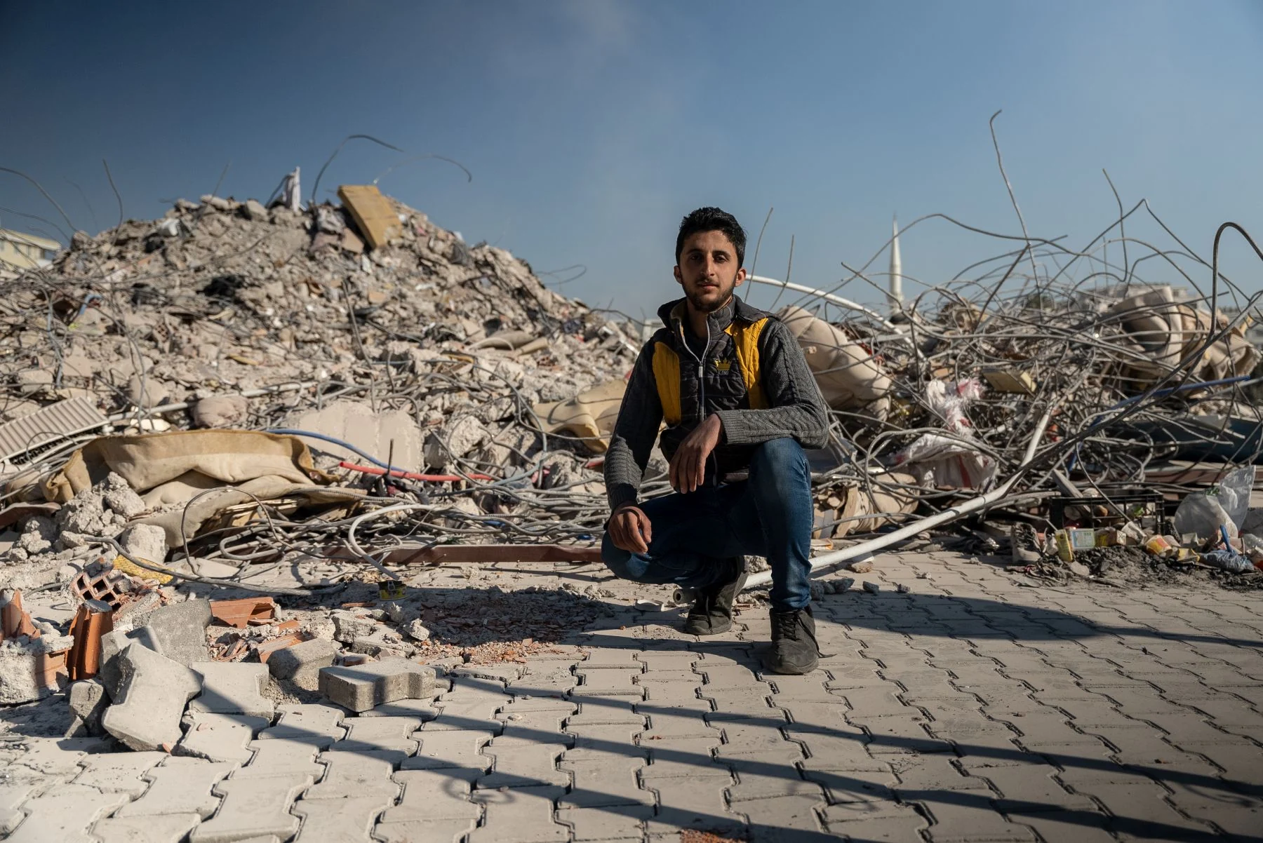 A young Syrian refugee kneels in front of rubble of a factory where he once worked before the earthquake.