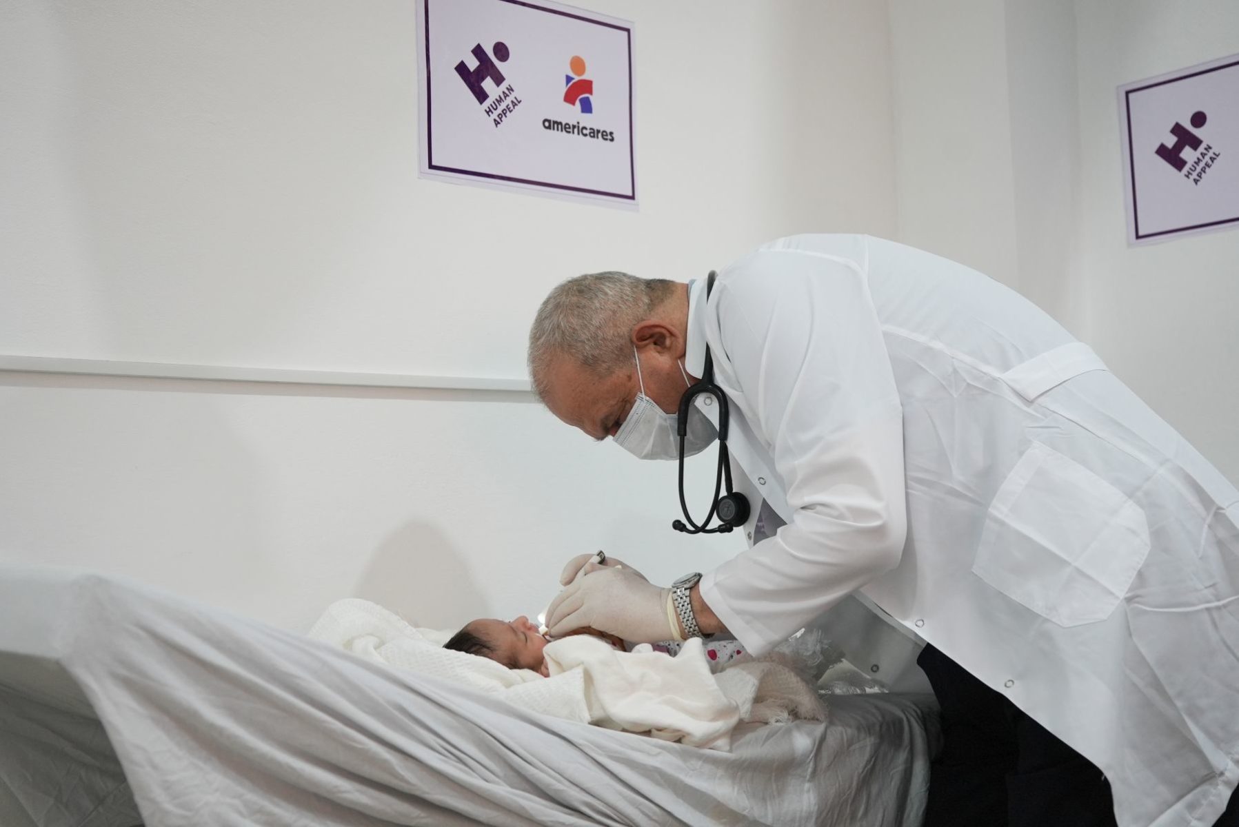 Doctor in white lab coat with mask and stethoscope examines a baby.
