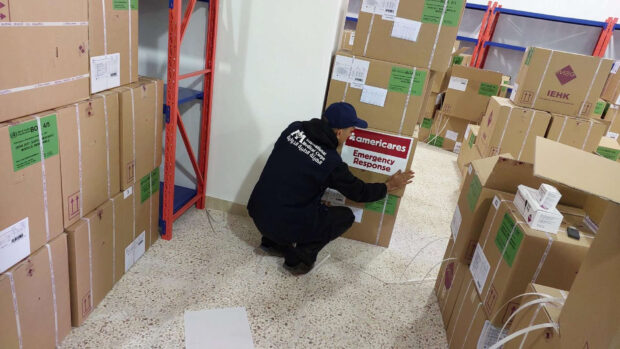 IMC worker in dark blue outfit places ameicares emergency response sign on part of the shipment in the warehouse.