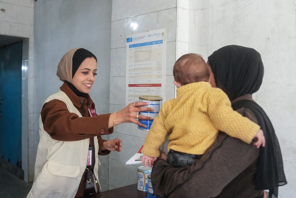 A staff member hands formula to a woman and child in Gaza
