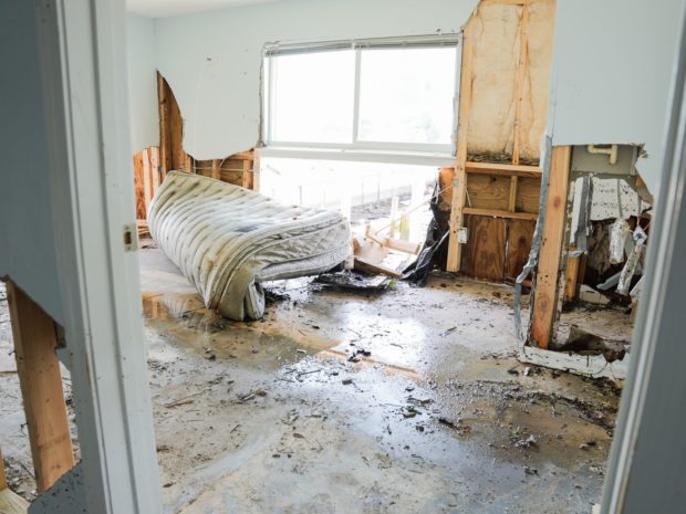 Interior of home damaged by Hurricane Idalia. Ruined, folded mattress lies on wet floor in front of window and surrounded by ruined walls with studs exposed behind sheet rock.