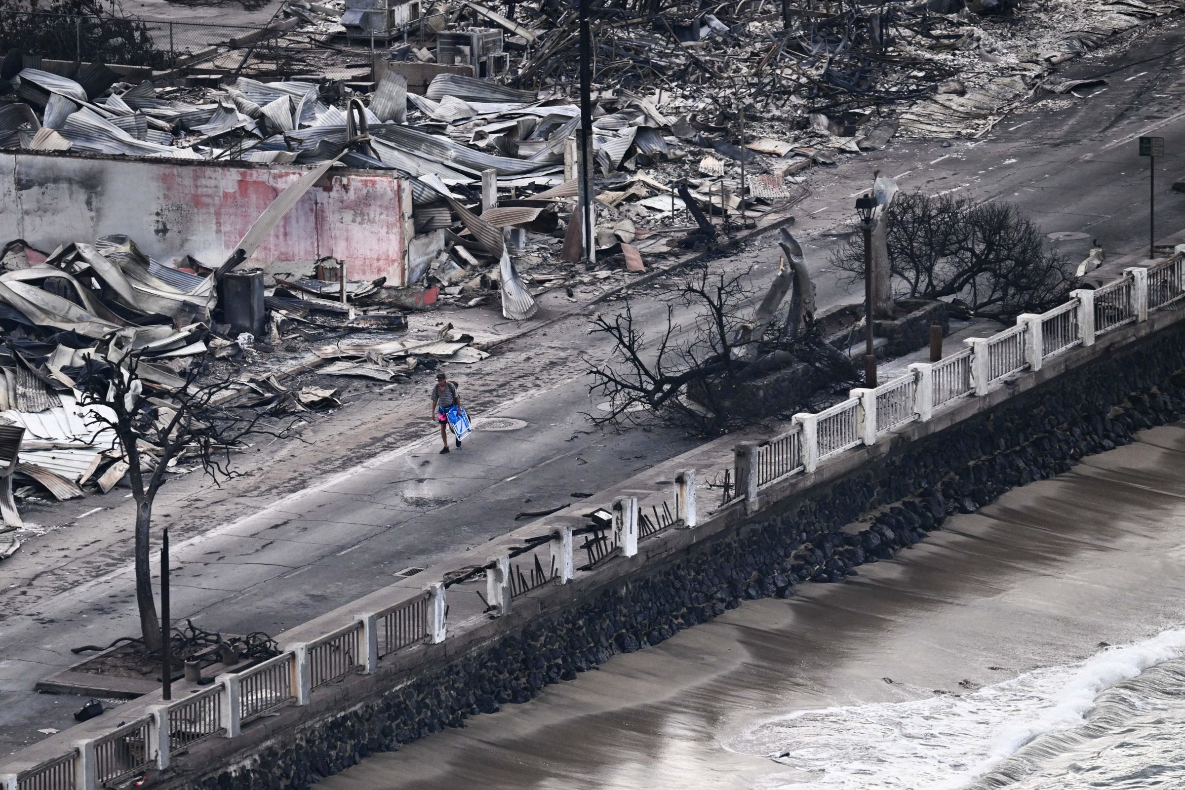 An aerial image taken on August 10, 2023 shows a person walking down Front Street past destroyed buildings burned to the ground in Lahaina in the aftermath of wildfires in western Maui, Hawaii. At least 36 people have died after a fast-moving wildfire turned Lahaina to ashes, officials said August 9, 2023 as visitors asked to leave the island of Maui found themselves stranded at the airport. The fires began burning early August 8, scorching thousands of acres and putting homes, businesses and 35,000 lives at risk on Maui, the Hawaii Emergency Management Agency said in a statement. (Photo by Patrick T. Fallon / AFP) (Photo by PATRICK T. FALLON/AFP via Getty Images)