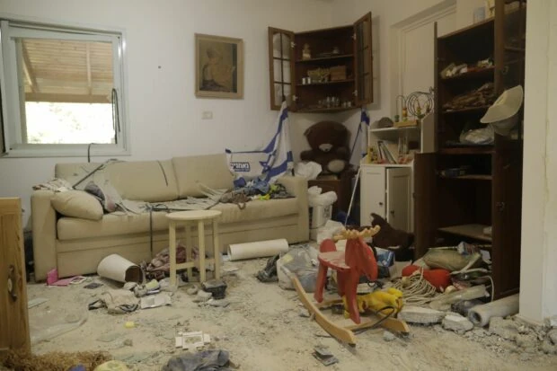 Interior of damaged home with child rocking horse, stuffed bear and an Israeli flag in the midst of much debris.