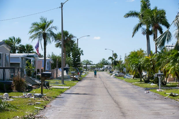 Person in storm damaged street in the distance with damaged houses and debris on either side.