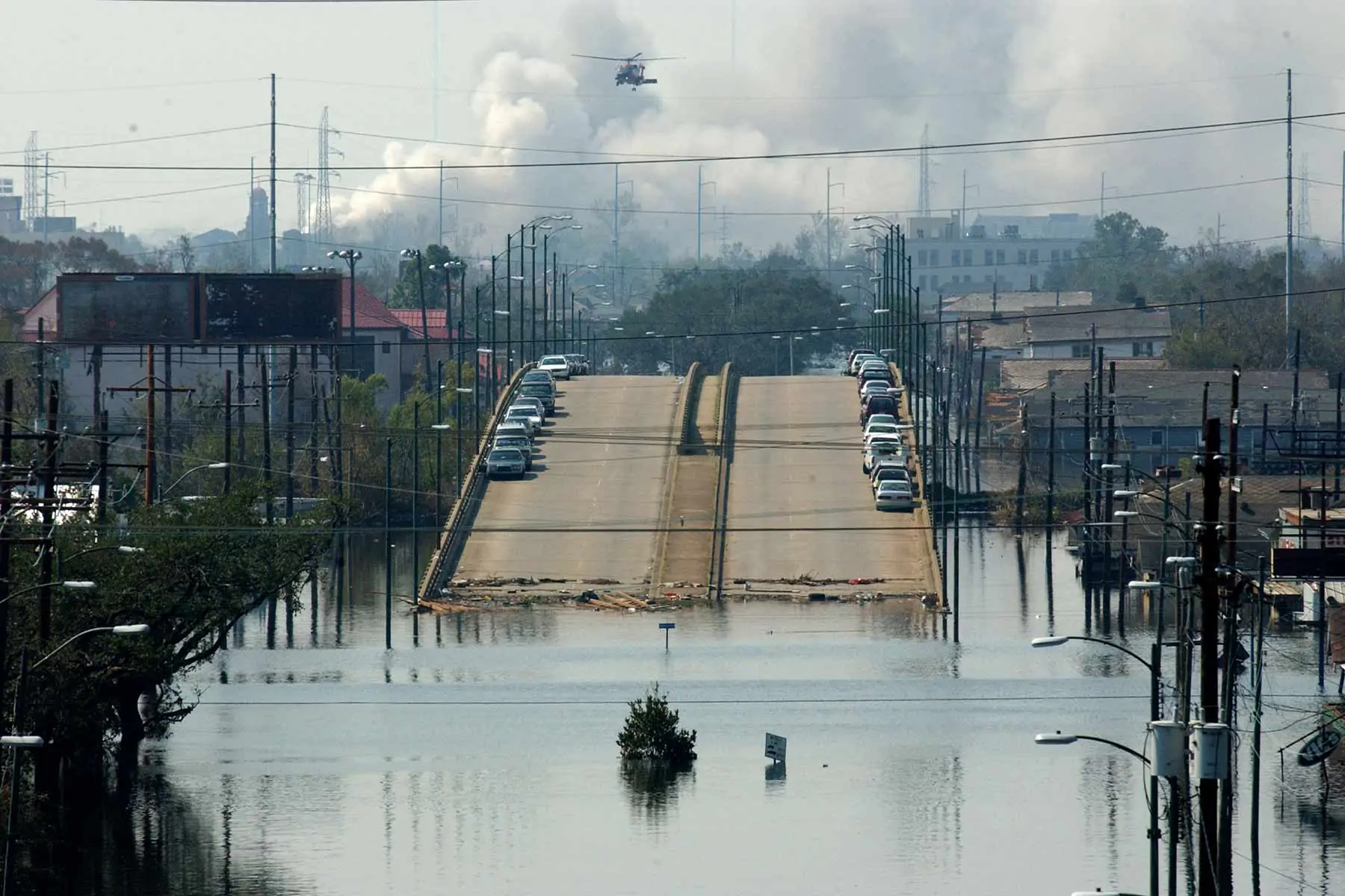 Flooding scene shows water up half way up street lamps with a bridge in the background and smoke.