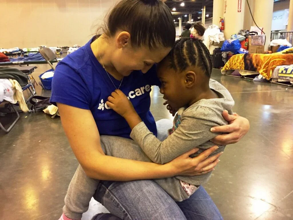 A young child plays with the necklace of an Americares worker as she holds her.