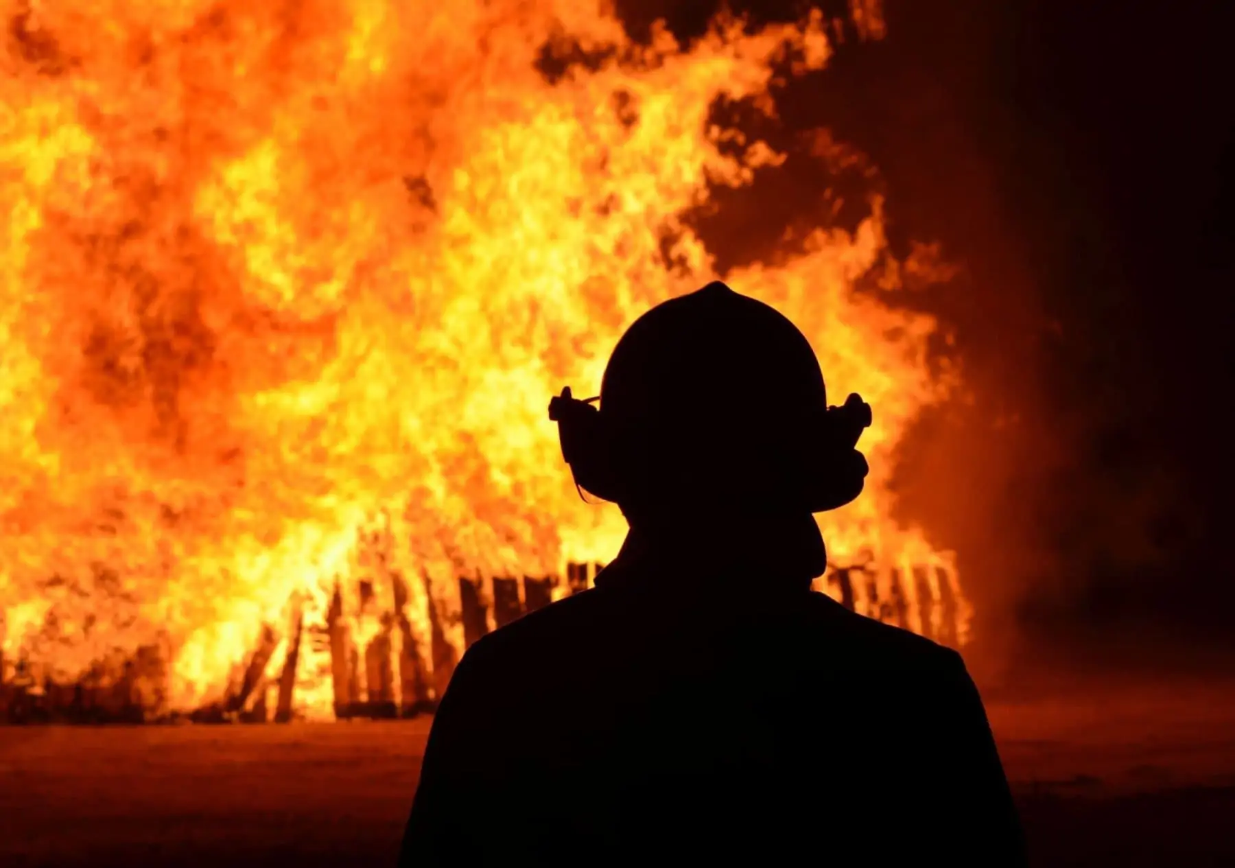 Silhouette of fireman watching huge flames in background