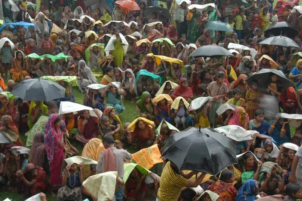 An overhead view of a crowd waiting in the rain with umbrellas and shalls covering their heads.